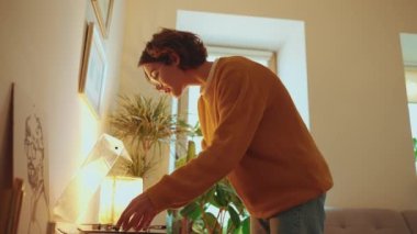Concentrated brunette woman wearing eyeglasses puts a vinyl record on the player at home 