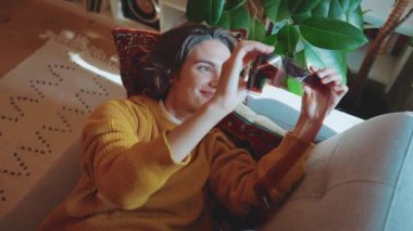 Positive brunette woman looking at old photos on film on the couch at home 
