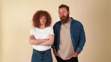 Bored red haired couple wearing casual clothes yawning in beige studio