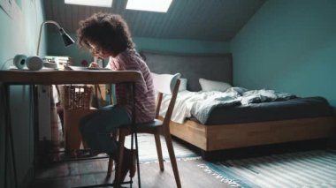 Concentrated curly haired young African girl does her homework at home