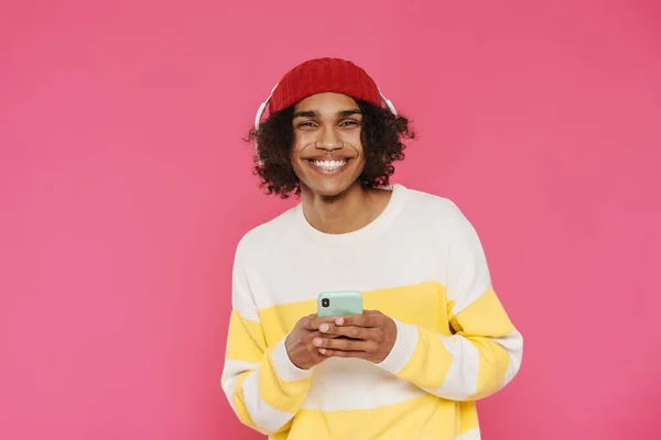 Young Caribbean Man Headphones Smiling Using Cellphone Isolated Pink Background — 图库照片