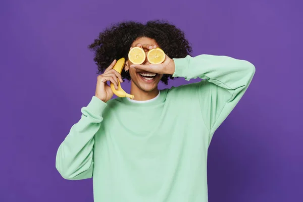 Young Caribbean Man Smiling While Making Fun Fruits Isolated Purple — Stockfoto