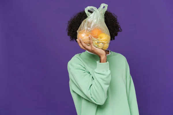 Young Caribbean Man Holding Showing Plastic Bag Fruits Isolated Purple — Stok fotoğraf