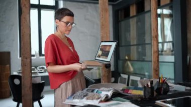 Confident brunette woman architect working on laptop and selects samples for interior design in the office