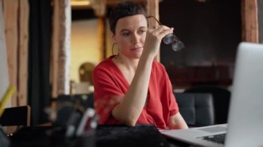 Cute brunette woman architect in eyeglasses working on laptop and looking at the camera in the office