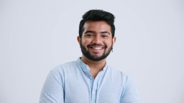 Smiling Indian man with piercing wearing blue shirt looking at the camera in the grey studio
