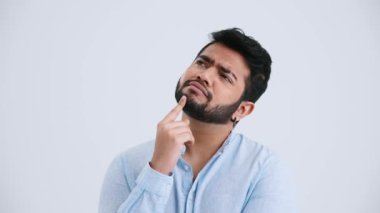 Concentrated Indian man with piercing wearing blue shirt thinking about something in the grey studio