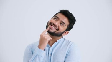 Pensive Indian man with piercing wearing blue shirt thinking about something in the grey studio