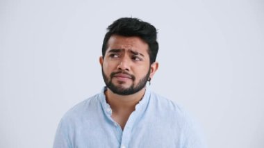 Confident Indian man with piercing wearing blue shirt disagrees with something in the grey studio