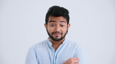 Positive Indian man with piercing wearing blue shirt agrees with something in the grey studio
