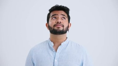 Happy Indian man with piercing wearing blue shirt looking around and at the camera in the grey studio
