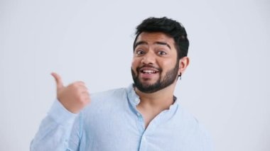 Happy Indian man with piercing wearing blue shirt pointing his finger at the copyspace in the grey studio