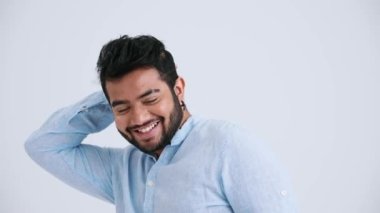 Handsome Indian man with piercing wearing blue shirt winking the camera in the grey studio