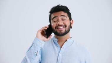 Happy Indian man with piercing wearing blue shirt talking on mobile in the grey studio