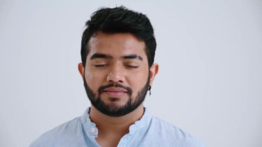 Lovely Indian man with piercing wearing blue shirt opening eyes at the camera in the grey studio