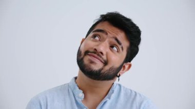 Meditative Indian man with piercing wearing blue shirt thinking about something in the grey studio