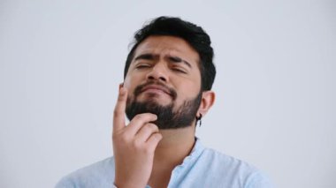 Confident Indian man with piercing wearing blue shirt thinks about something and has an idea in the grey studio