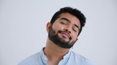 Bored Indian man with piercing wearing blue shirt looking around and at the camera in the grey studio