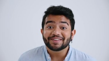 Surprised Indian man with piercing wearing blue shirt rejoicing at the camera in the grey studio