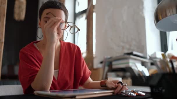 タブレットやオフィスのコーヒーを飲む上で作業眼鏡で短い髪の疲れ女性建築家 — ストック動画