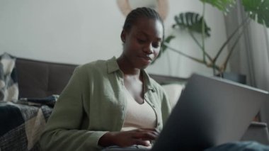 Confident African woman with pigtails working on laptop at home