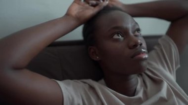 Disaffected African woman with pigtails and depression looking around on the couch at home