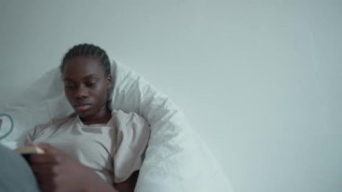 Upset African woman with pigtails and depression reading book on the bed at home