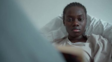 Confident African woman with pigtails and depression reading book on the bed at home