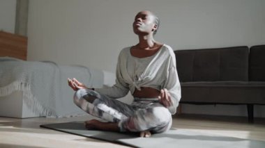 Concentrated African woman with pigtails does yoga meditation on the mat at home