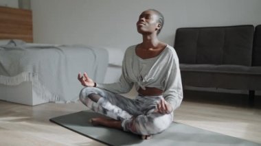 Smiling African woman with pigtails does yoga meditation on the mat at home