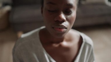 Serious African woman with pigtails does yoga meditation and looking at the camera at home