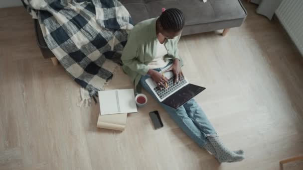 深刻なアフリカ人女性とともにピグテール作業ノートパソコン上で座っている間に床に自宅 — ストック動画