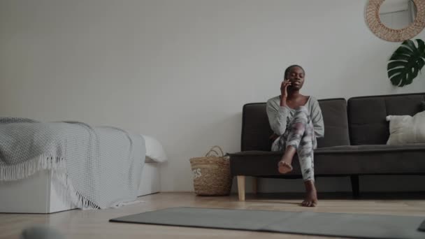 ハンサムなアフリカ人女性ですピグテールとともにモバイル上のソファに自宅で — ストック動画