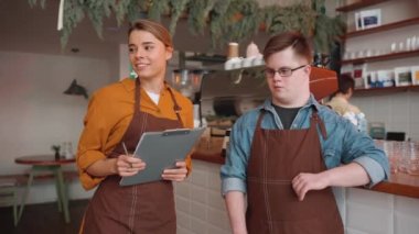 Confident male waiter with Down syndrome talking to a girl colleague in the cafe