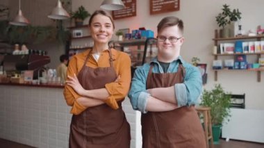 Happy male waiter with Down syndrome standing with a girl colleague and looking at the camera in the cafe