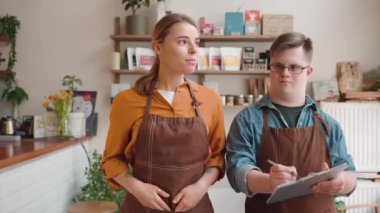 Concentrated man waiter with Down syndrome listening his girl colleague and walking in the cafe