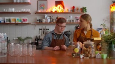 Pensive man waiter with Down syndrome talking with his girl colleague at the cash register in a cafe