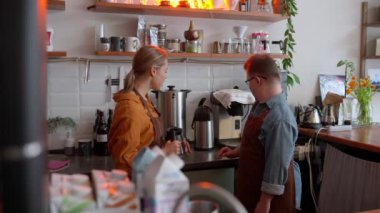 Confident man barista with Down syndrome studying the coffee machine with his girl colleague in a cafe