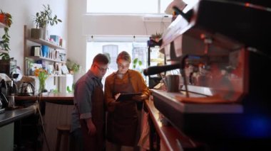 Pensive man barista with Down syndrome reading book and talking with his girl colleague in a cafe