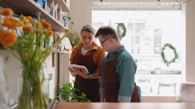 Serious man barista with Down syndrome listening his girl colleague about coffee in a cafe
