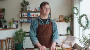 Happy man barista with Down syndrome looking at window and at camera in cafe