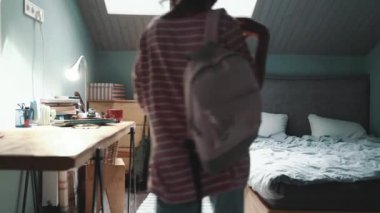 Handsome curly haired young African girl typing on mobile in headphones after walking on the bed at home