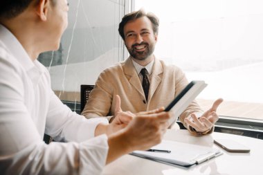 Adult multiracial businessmen talking and using tablet computer while sitting by table indoors