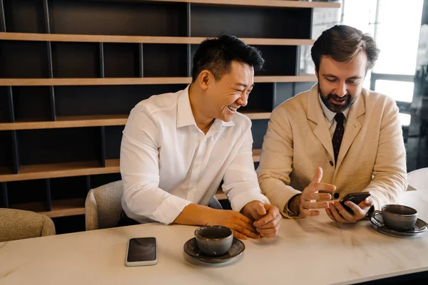Two Middle Aged Businessmen Look Phone Discuss Sitting Table Cups — Stock Photo, Image