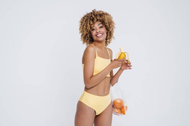 Young black woman wearing underclothes smiling and holding bag with fruits isolated over white background