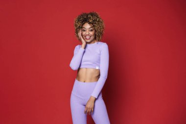 Young black woman with afro curls smiling and posing at camera isolated over red background