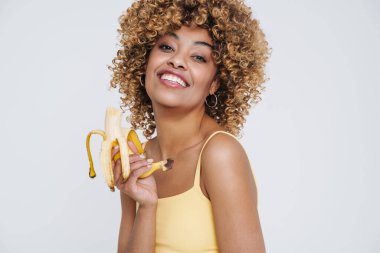 Young black woman wearing underclothes smiling and holding banana isolated over white background