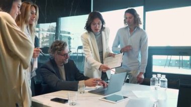 Concentrated professional employees and managers talking about work and looking at laptop at the office table