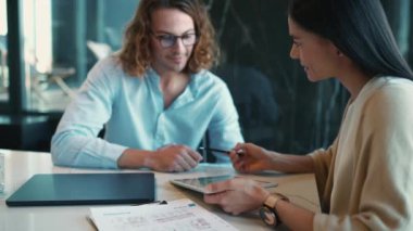 Smiling woman and man managers working on tablet and talking while sitting in the office