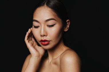Young asian shirtless woman wearing makeup posing at camera isolated over black background